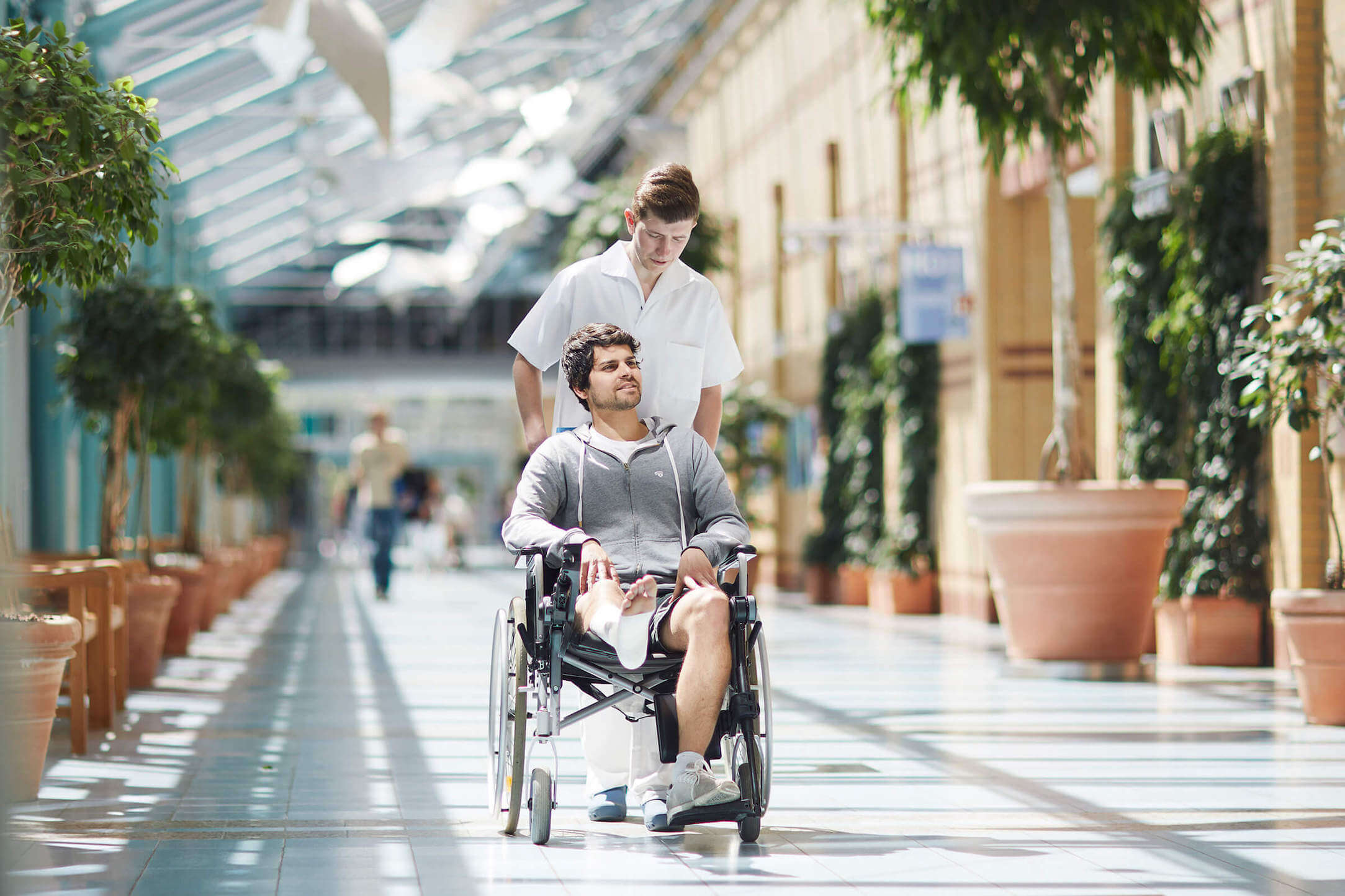 Caregiver is pushing a man in a wheelchair through the lobby