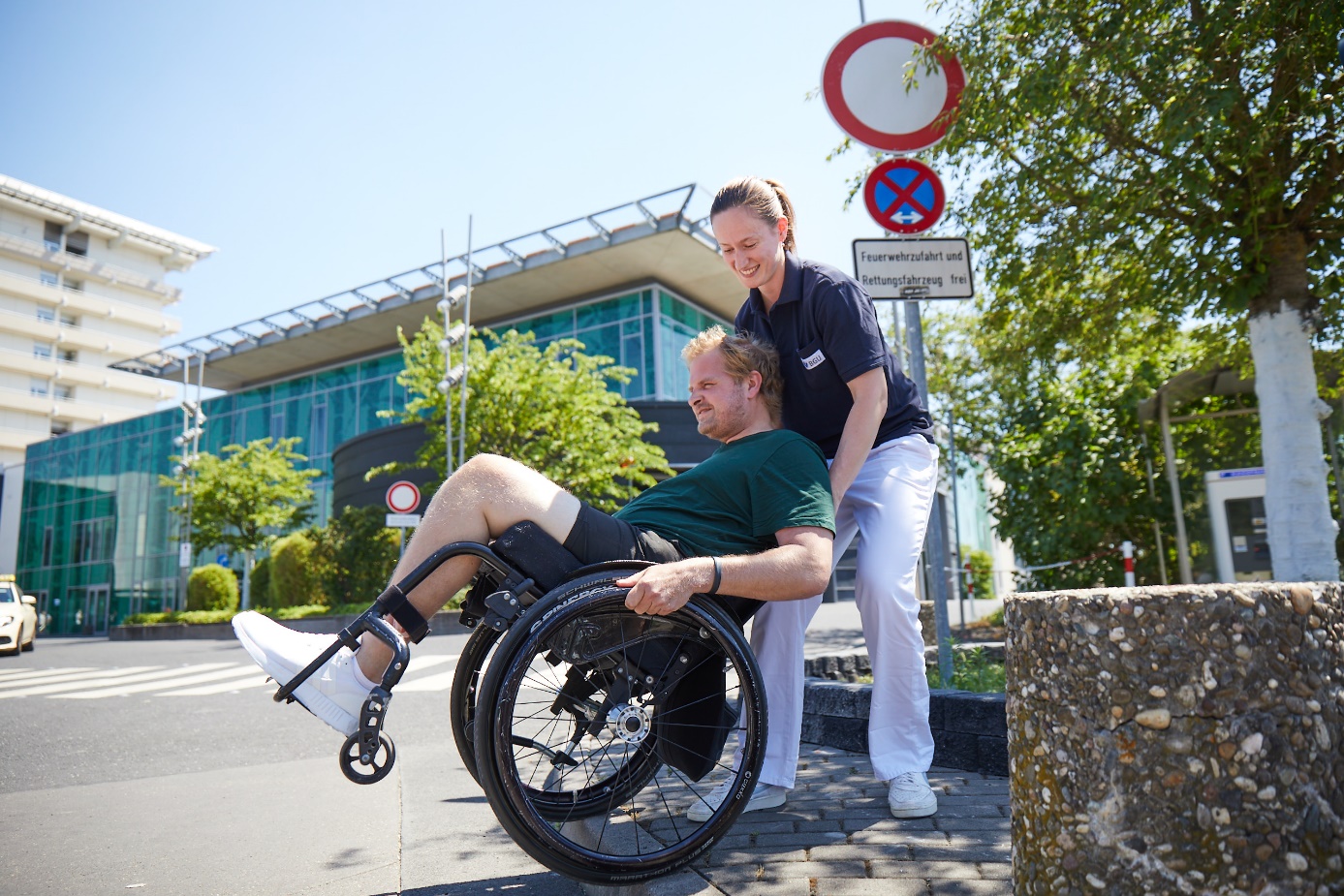 Rollstuhl-Training an Bordsteinkante vor der Klinik