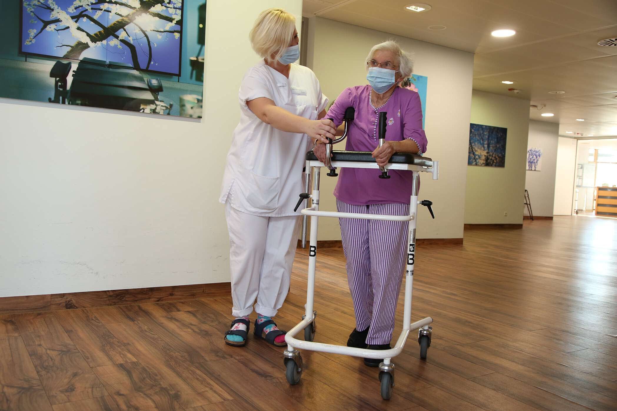 Alte Frau mit Rollator wird von Pflegefachkraft geführt