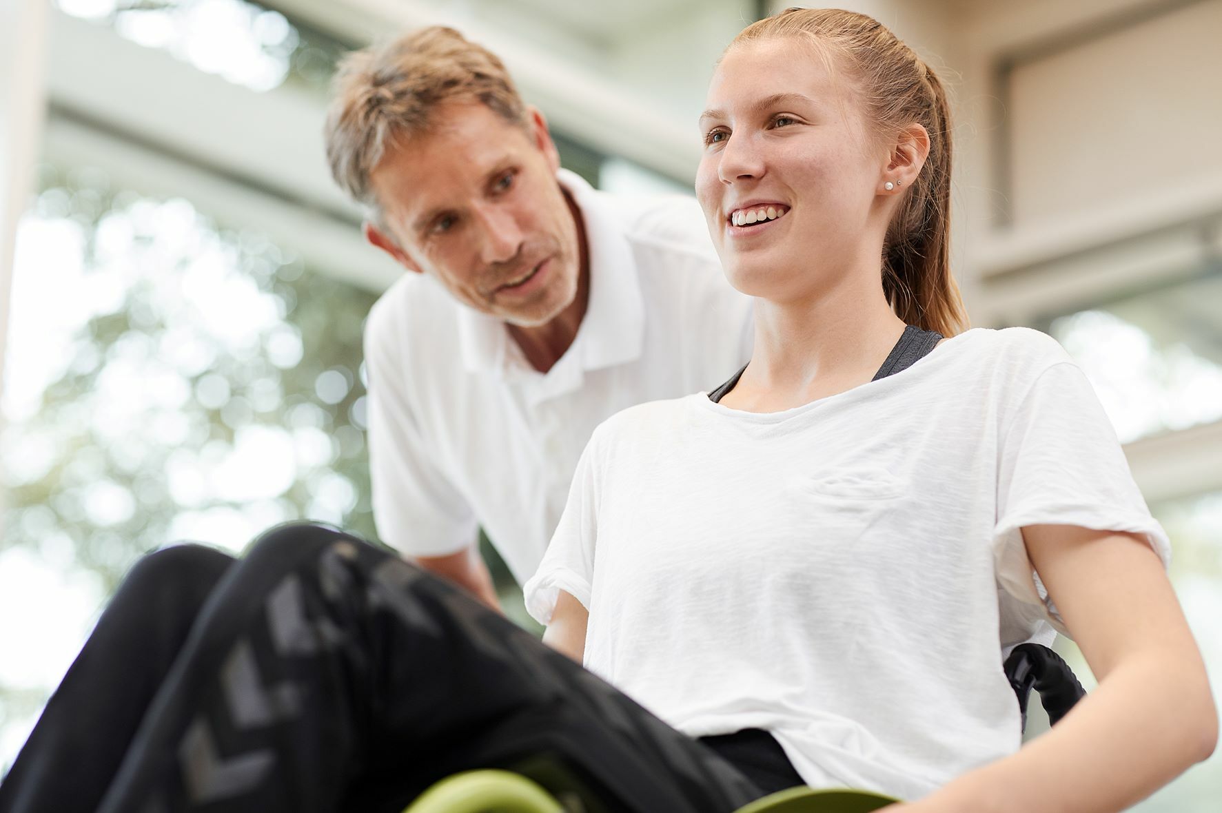 BG Kliniken - Unser Auftrag Pfleger spricht mit Patientin im Rollstuhl
