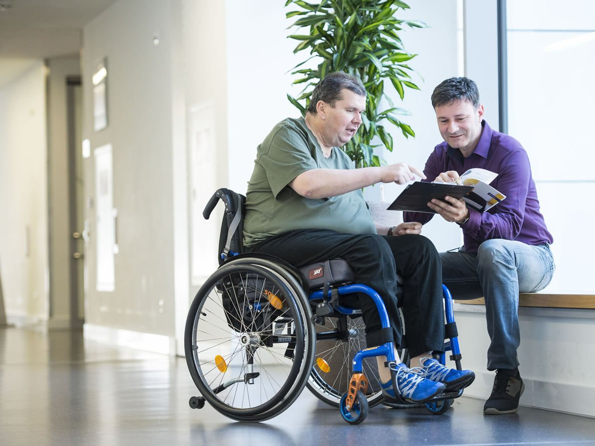 Herr Schaller vom Sozialdienst und ein Patient im Rollstuhl im Gespräch Foto im Gespräch mit Patienten im Rollstuhl