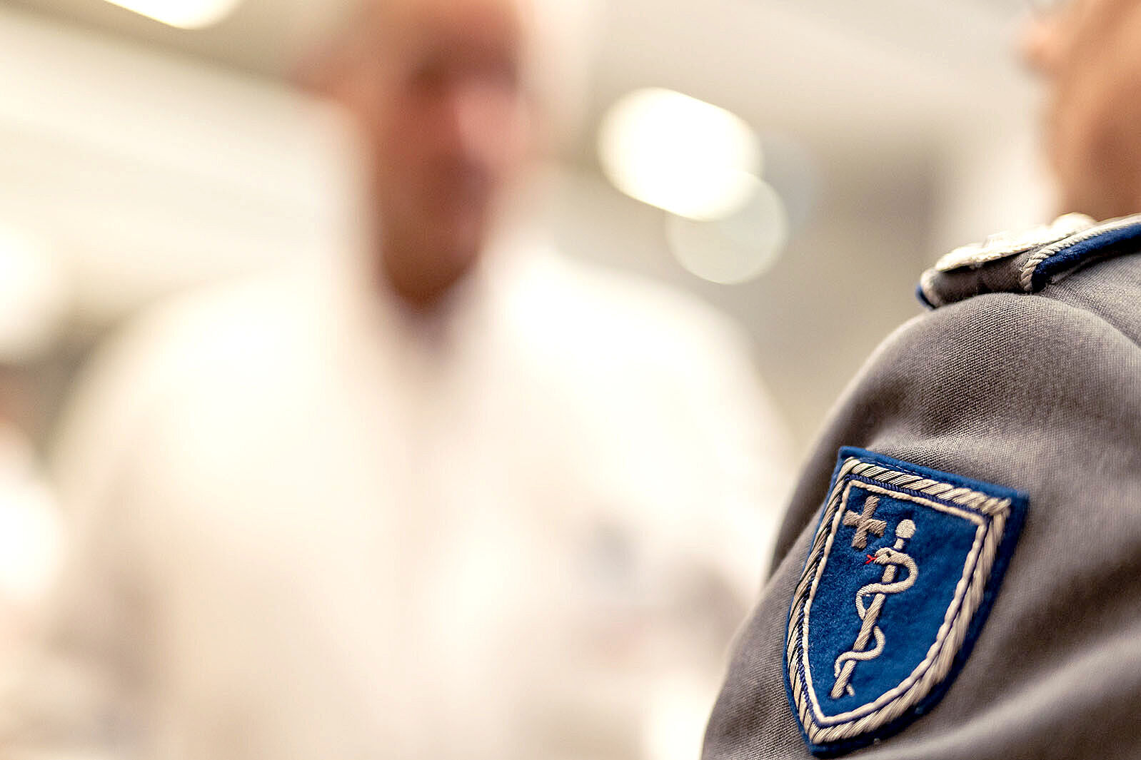 Im Hintergrund ein Mediziner der BG Kliniken, im Vordergrund das Abzeichen des Sanitätsdiensts der Bundeswehr