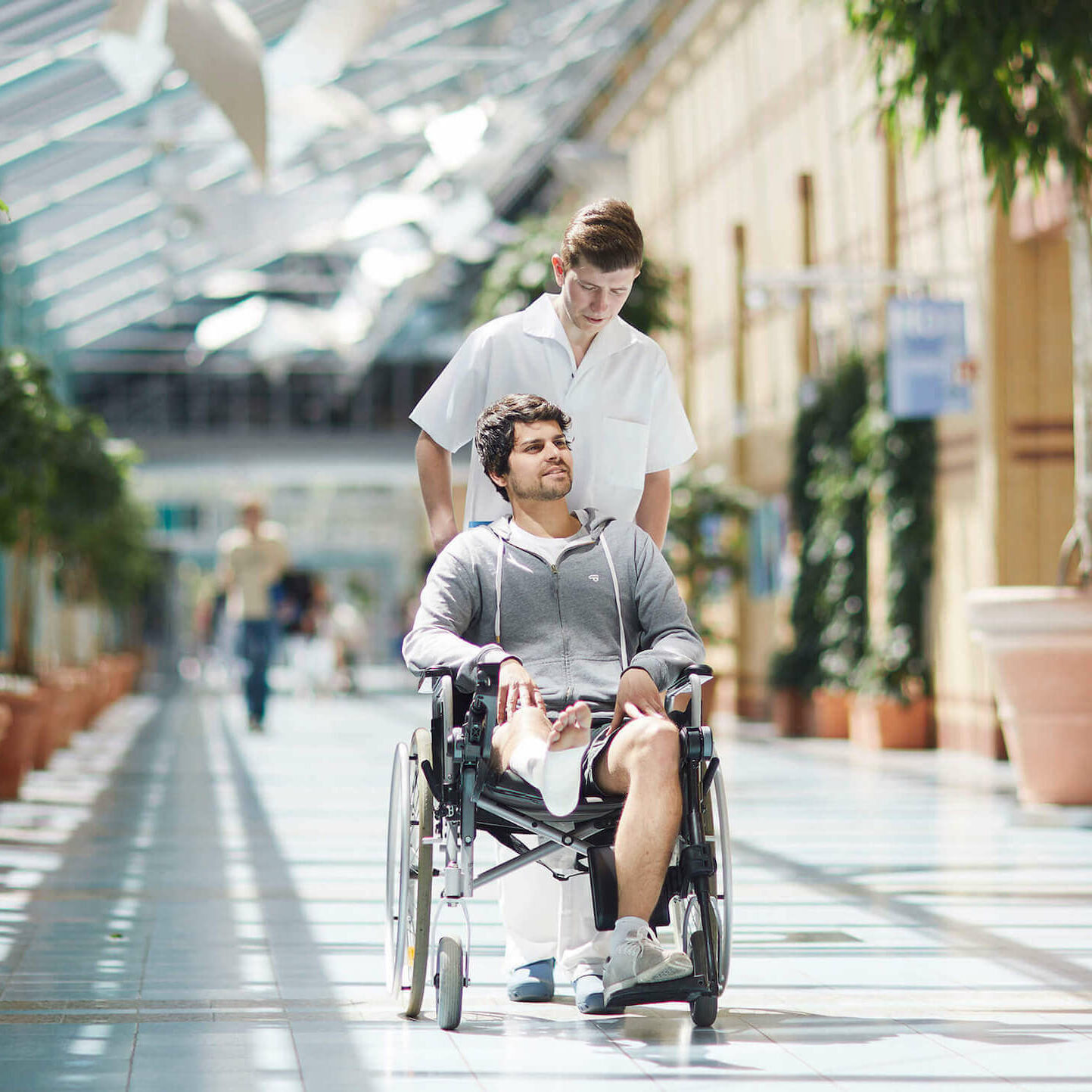 Ein Pfleger schiebt einen Patienten mit Gips am Bein im Rollstuhl