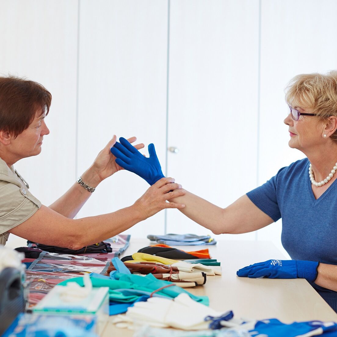 Eine Therapeutin berät eine Patientin, welche Handschuhe sie bei der Arbeit tragen soll